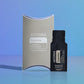 doTERRA Copaiba .25 mL black sample sachet standing beside its taupe doTERRA pillow box on a glossy blue studio surface with soft reflections. doTERRA Copaiba Essential Oil Sample (.25 mL)