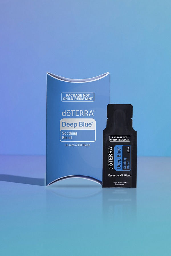 doTERRA Deep Blue Soothing Blend .25 mL black sample sachet standing beside its blue doTERRA pillow box on a glossy blue studio surface with soft reflections. doTERRA Deep Blue Essential Oil Sample (.25 mL)