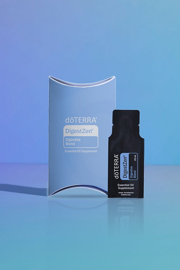 doTERRA DigestZen Digestive Blend .25 mL black sample sachet standing beside its light blue doTERRA pillow box on a glossy blue studio surface with soft reflections. doTERRA DigestZen Essential Oil Sample (.25 mL)