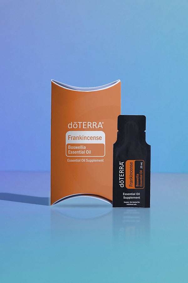 doTERRA Frankincense .25 mL black sample sachet standing beside its orange doTERRA pillow box on a glossy blue studio surface with soft reflections. doTERRA Frankincense Essential Oil Sample (.25 mL)