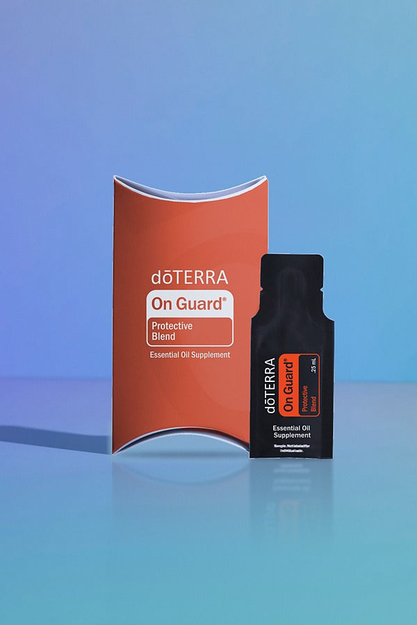 doTERRA On Guard Protective Blend .25 mL black sample sachet standing beside its red-orange doTERRA pillow box on a glossy blue studio surface with soft reflections. doTERRA On Guard Essential Oil Sample (.25 mL)