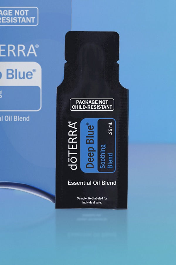 Close-up of the doTERRA Deep Blue Soothing Blend .25 mL black sample sachet standing upright in front of its blue pillow box on a blue background. doTERRA Deep Blue Essential Oil Sample (.25 mL)
