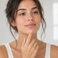 Woman at a bright bathroom mirror dabbing doTERRA Tea Tree on her chin with a fingertip. doTERRA Tea Tree Essential Oil Sample (.25 mL)