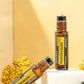 Two amber glass roll-on bottles of doTERRA Helichrysum essential oil, one standing upright on a white block and one lying diagonally, with yellow flowers against a warm beige background.