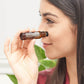 A woman holds a small amber glass bottle near her nose, showing the label which reads 'Sopapila' and 'COPPER'.