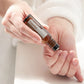 A person's hands holding a small amber roll-on bottle labeled 'DROPSA Copaliba' over their palm, with a soft white robe in the background.