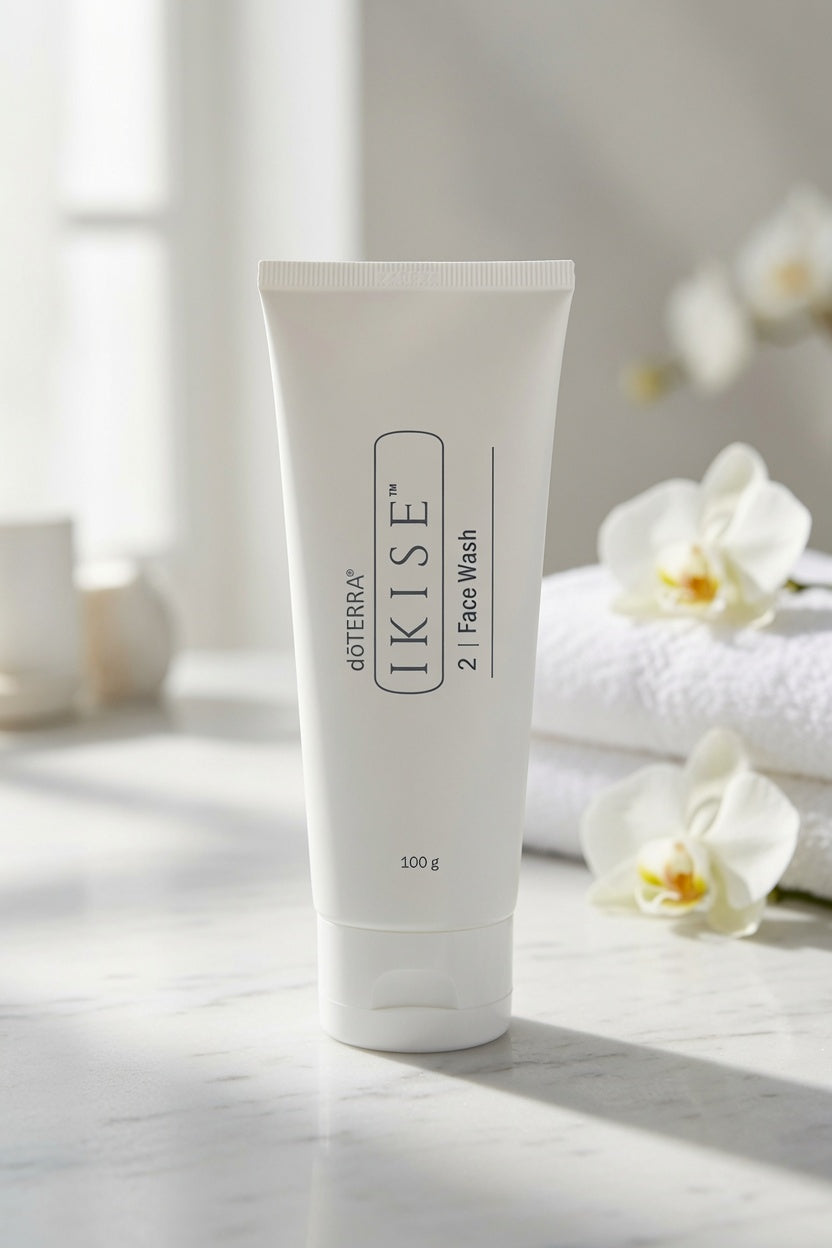 A 100g white squeeze tube of Goterra I Kise 2 Face Wash standing on a marble surface, with soft-focus white orchids and folded towels in the background.