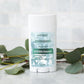A white doTERRA Deodorant stick with a blue and green label, standing on a light marble surface with eucalyptus leaves around it.