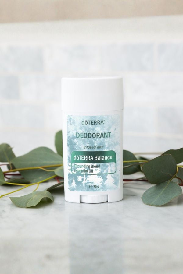 A white doTERRA Deodorant stick with a blue and green label, standing on a light marble surface with eucalyptus leaves around it.