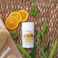 A doTERRA Skin & Scense body care product stick sits on a woven straw mat, surrounded by orange slices, green leaves, and bath sponge props.