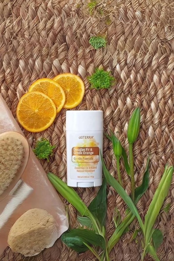 A doTERRA Skin & Scense body care product stick sits on a woven straw mat, surrounded by orange slices, green leaves, and bath sponge props.