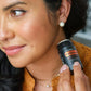 A woman holding a black Osterixx FaceMinimizing Deodorant stick next to her ear, wearing a textured orange top.