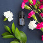 A small amber essential oil bottle labeled 'Pleasant Valley' is arranged on a dark blue textured surface with white and pink flowers and green leaves  doTERRA Juniper Berry Essential Oilaround it.