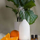 A white essential oil diffuser with misting at the top, styled with orange slices, a whole orange, and two amber dropper bottles on a draped white fabric surface with a potted green plant in the background. doTERRA LaLuz Diffuser