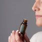 A close-up lifestyle shot of a woman holding a small amber glass bottle of doTERRA Eucalyptus essential oil, with her face partially visible in profile against a solid gray background.
