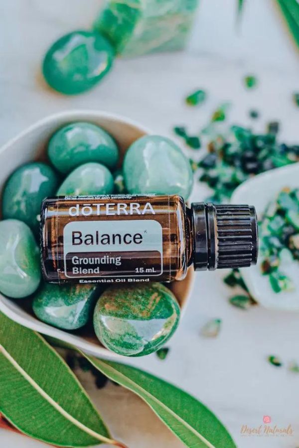 A bottle of doTERRA Balance Grounding Blend essential oil surrounded by green stones and leaves in a styled flat-lay arrangement.