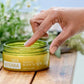 Hand reaching for a jar of doTERRA body scrub on a wooden surface with a natural background.