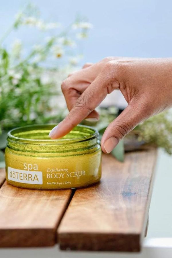 Hand reaching for a jar of doTERRA body scrub on a wooden surface with a natural background.
