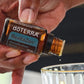Hand adding a drop of doTERRA RevitaZen Detoxification Blend to a glass of water