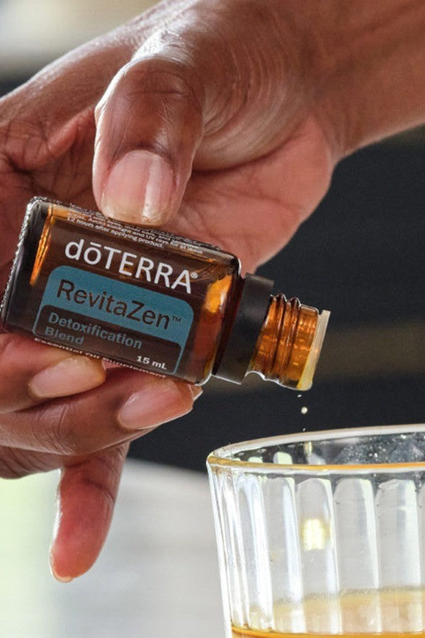 Hand adding a drop of doTERRA RevitaZen Detoxification Blend to a glass of water