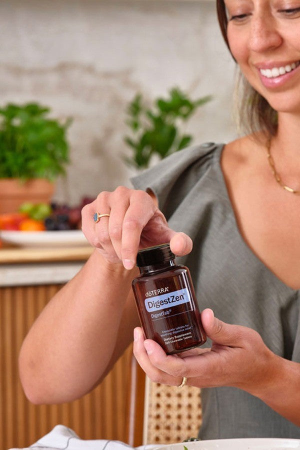 Smiling woman opening a bottle of doTERRA DigestTab Chewable Tablets in the kitchen