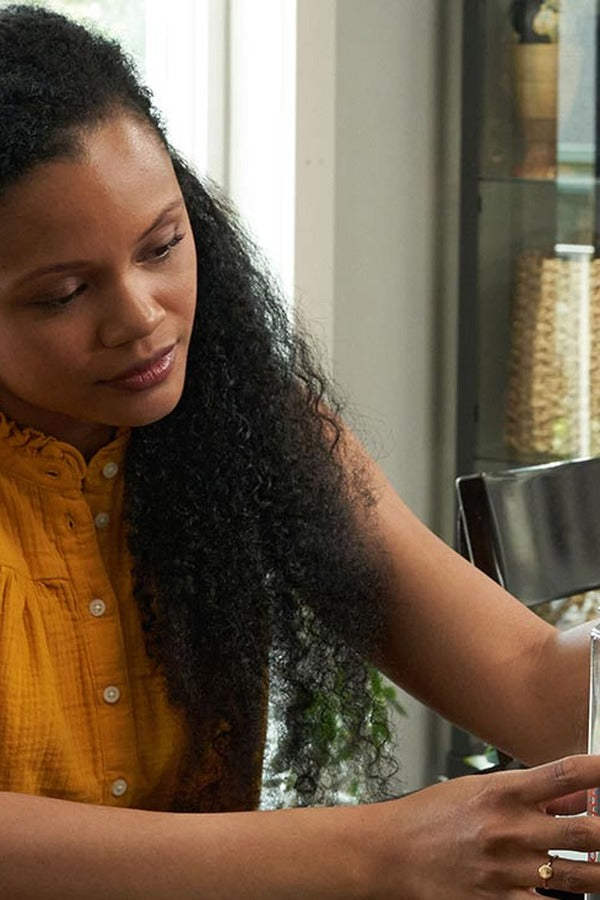 Woman mixing a doTERRA MetaPWR Advantage stick pack into a glass of water at her table