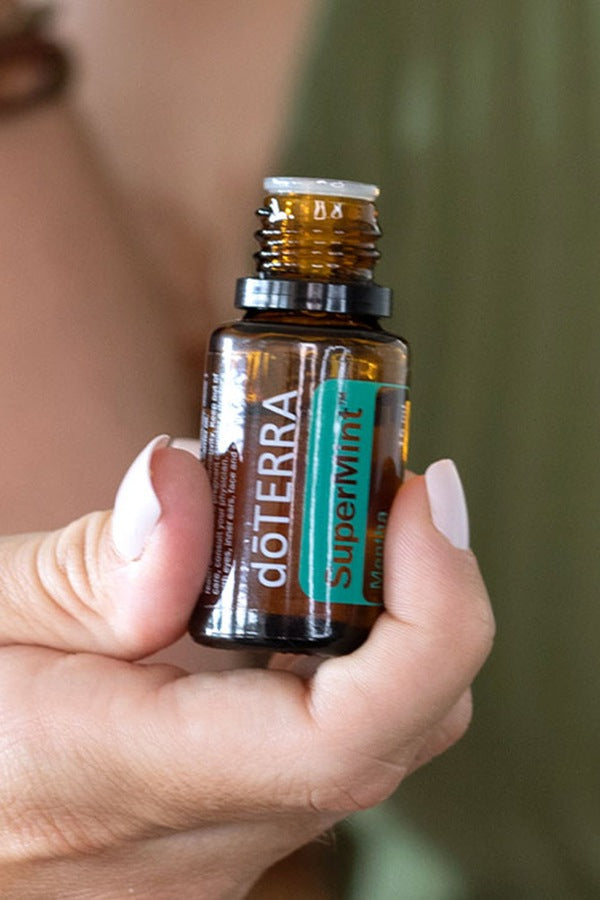 Hand holding a doTERRA SuperMint 15 mL essential oil bottle