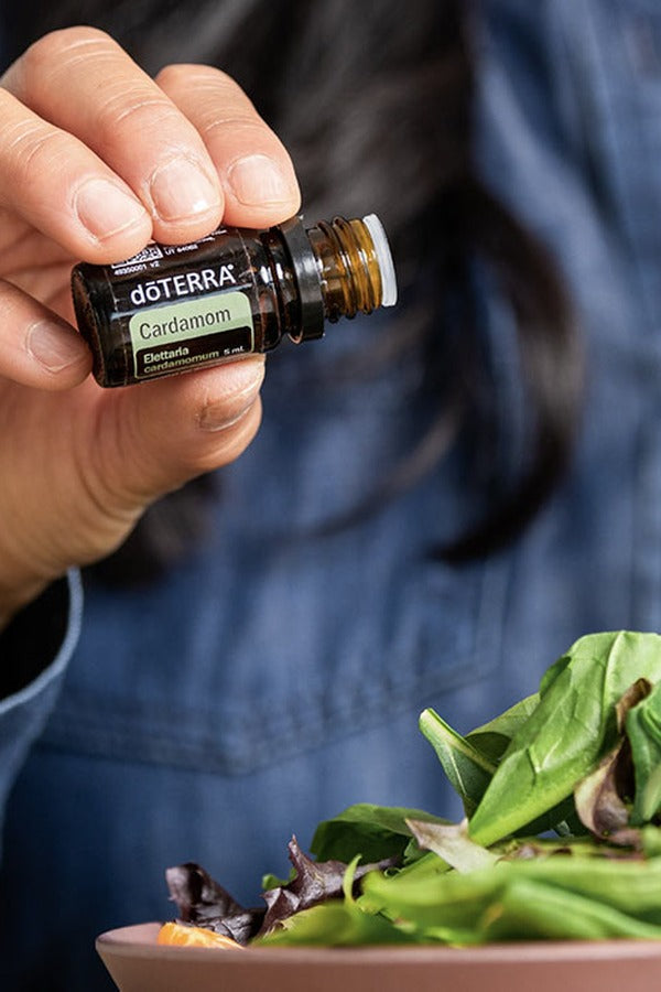 Hand adding doTERRA essential oil to a fresh salad