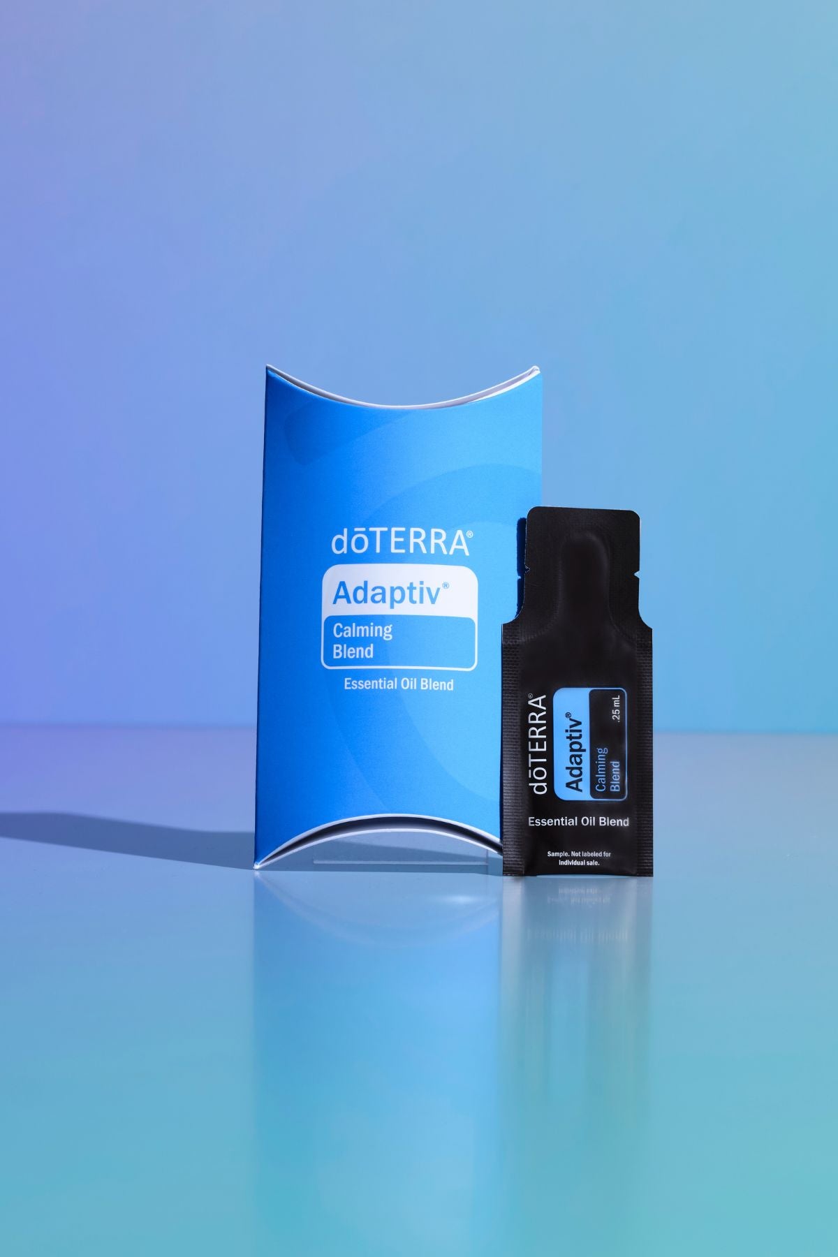 A doTERRA Adaptiv Grooming Blend essential oil blend set, featuring a blue curved box and a black single-use sachet, displayed on a reflective light blue surface against a blue gradient background. doTERRA Adaptiv Essential Oil Sample (.25 mL)