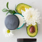 Two jars of Doterra body butter with an avocado and flowers on a light background