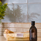 A bottle of doTERRA coconut oil stands on a countertop next to a folded doTERRA pouch, with a wooden brush in a bowl in the background against a tiled wall.