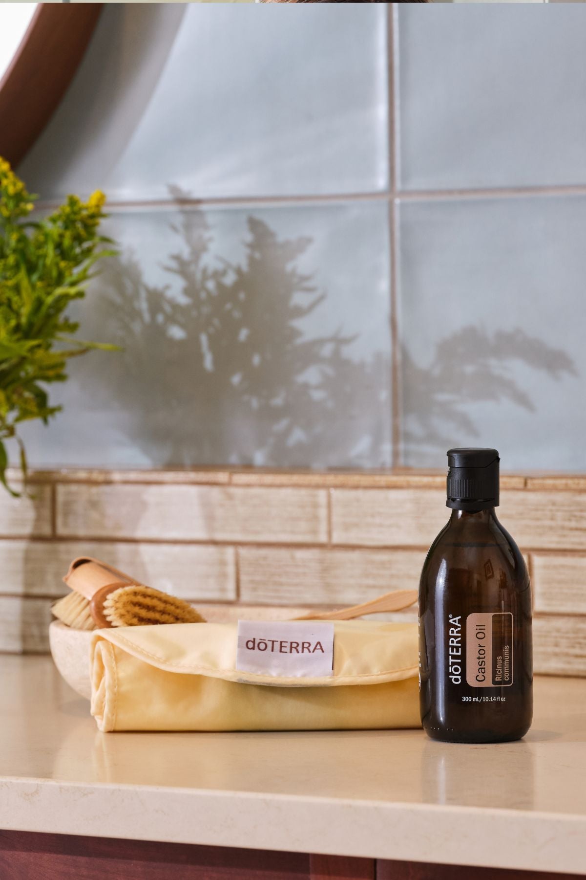 A bottle of doTERRA coconut oil stands on a countertop next to a folded doTERRA pouch, with a wooden brush in a bowl in the background against a tiled wall.