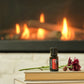 A small bottle of doTERRA cat spray placed on a stack of books in front of a warm fireplace, with a flower resting beside it.