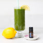 A tall glass mug filled with a bright green juice, set on a white surface with a fresh lemon, a small essential oil bottle, and a candle on a white background. doTERRA Juniper Berry Essential Oil