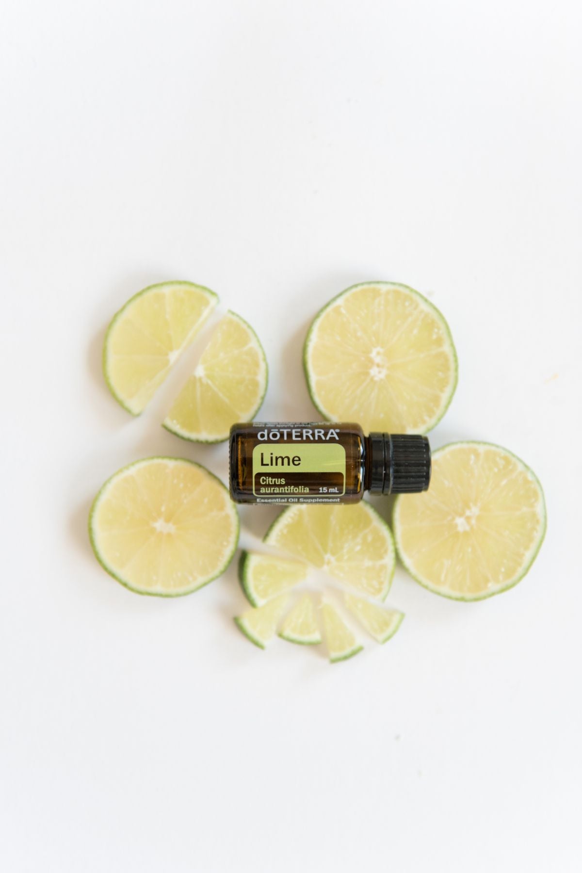 A bottle of doTERRA Lime essential oil surrounded by fresh lime slices on a clean white background.