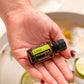A hand holding a small bottle of doTERRA Lime Cellar Botanicals essential oil over a bowl of citrus slices and herbs.