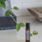 A small amber roll-on bottle labeled doTERRA Peppermint sits on a light countertop, with a trailing green plant and a neutral interior background visible.