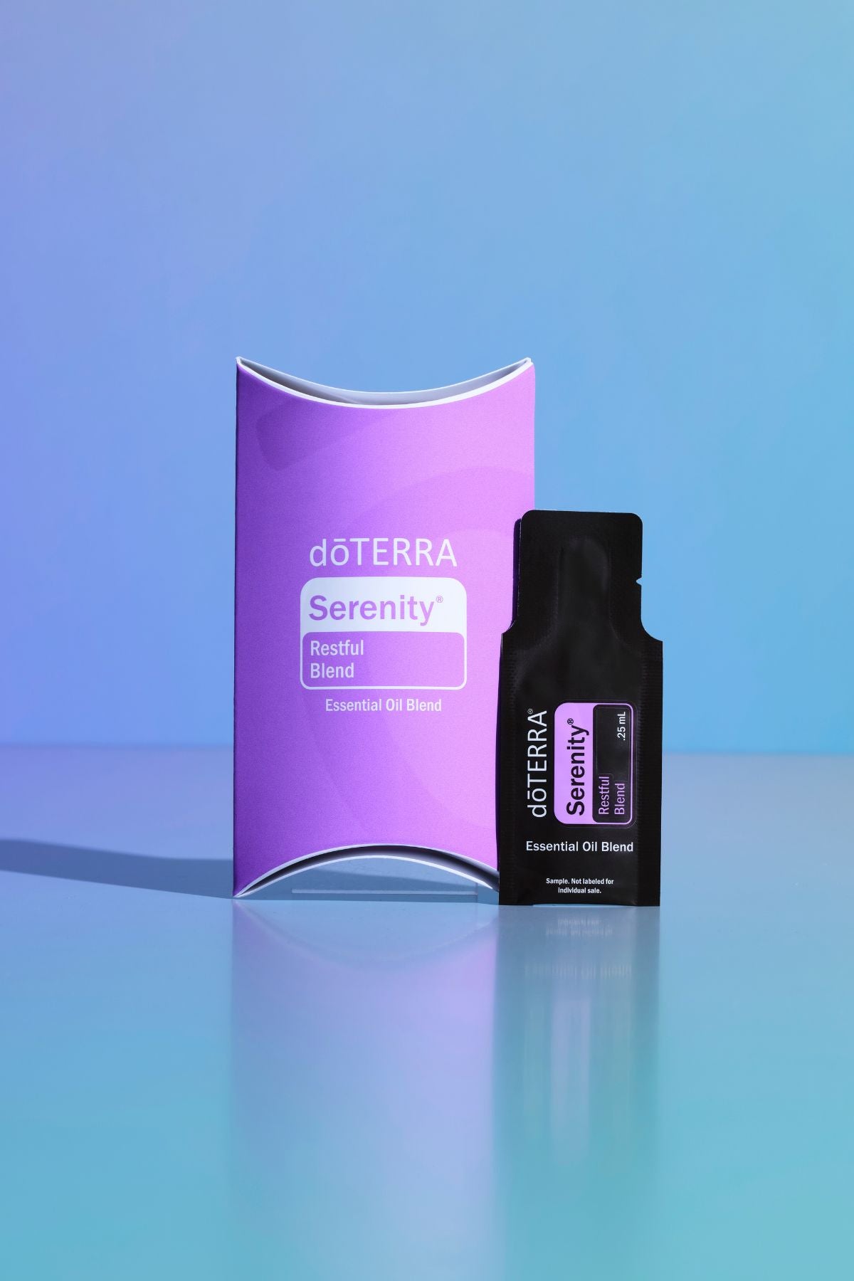 A dOTERRA Serenity Respiratory Blend essential oil blend set, featuring a purple curved box and a black single-serve packet, displayed on a reflective light blue surface against a blue gradient background. doTERRA Serenity Essential Oil Sample (.25 mL)