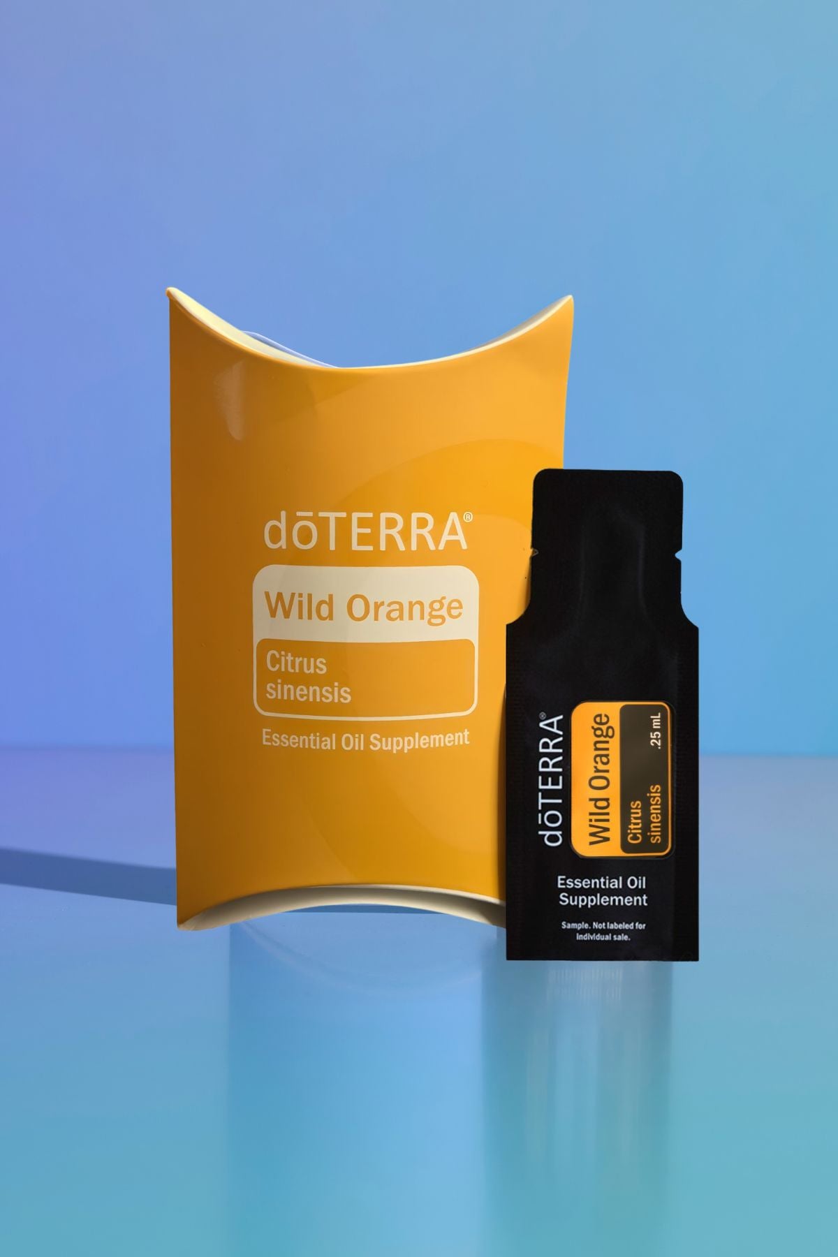 A doTERRA Wild Orange essential oil supplement set featuring a large yellow-orange curved box and a smaller black single-use sachet, displayed on a reflective light blue surface against a blue gradient background. doTERRA Wild Orange Essential Oil Sample (.25 mL)