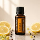 A bottle of doTERRA Litsea essential oil centered on a light stone surface, surrounded by lemon slices, small yellow flowers, and scattered peppercorns. The amber glass bottle has a black cap and a black-and-orange label with the doTERRA brand and 'Litsea' visible.